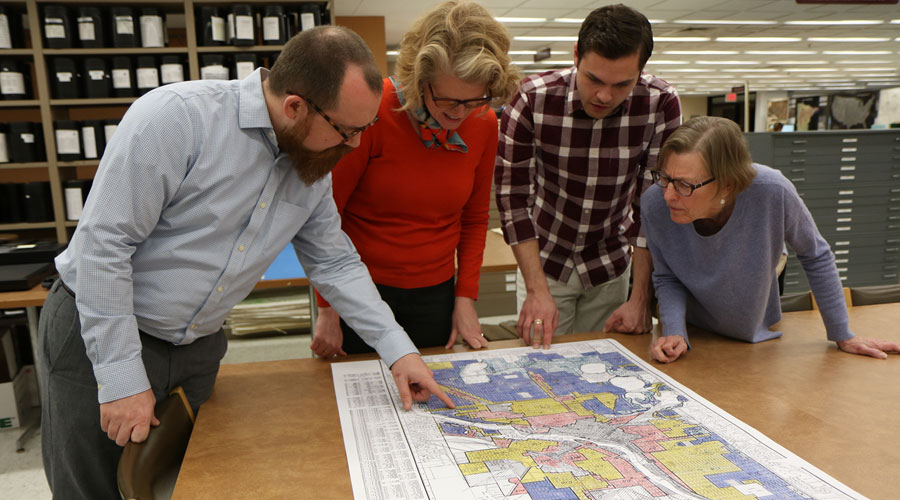 Four people standing around a table pointing at a map